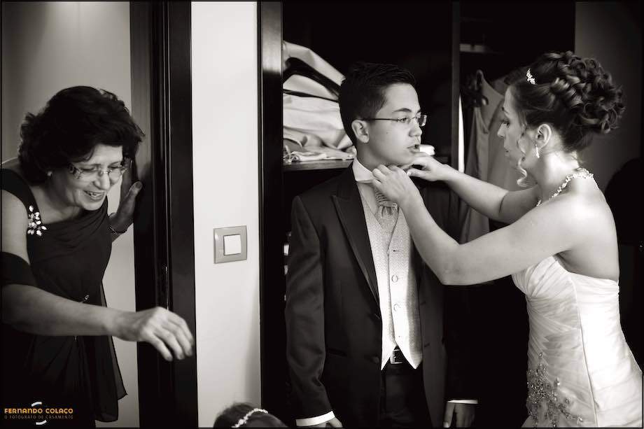 The bride hits her son's tie while her mother chats with her granddaughter, outside the image, seen by the Lisbon wedding photographer.