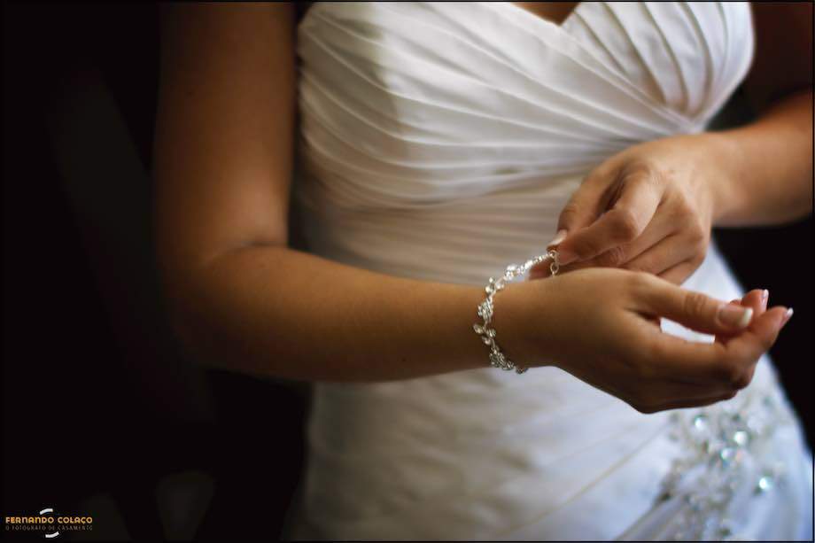 Hands of the bride putting the bracelet on her wrist, in a Lisbon wedding photographer composition.
