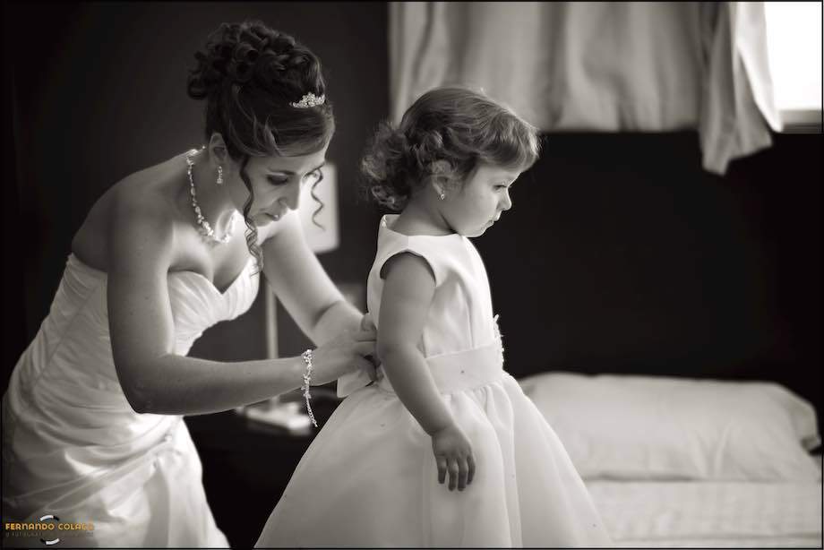 The bride, and mother, fastens her little girl's dress to go to the wedding ceremony, as seen by their wedding photographer in Lisbon.
