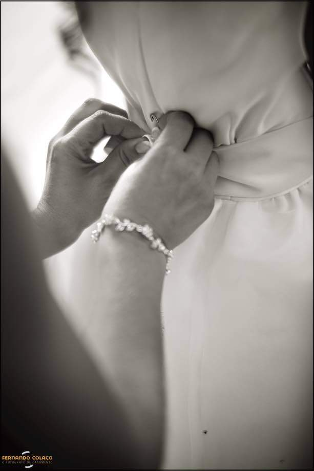 The bride's hands press the buttons of her little daughter's dress, moments before they leave for the wedding ceremony, by the Lisbon wedding photographer.
