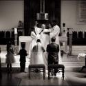 During the wedding ceremony, the priest blessing the bride and groom kneeling in front of the altar, captured by the wedding photographer in Oeiras.