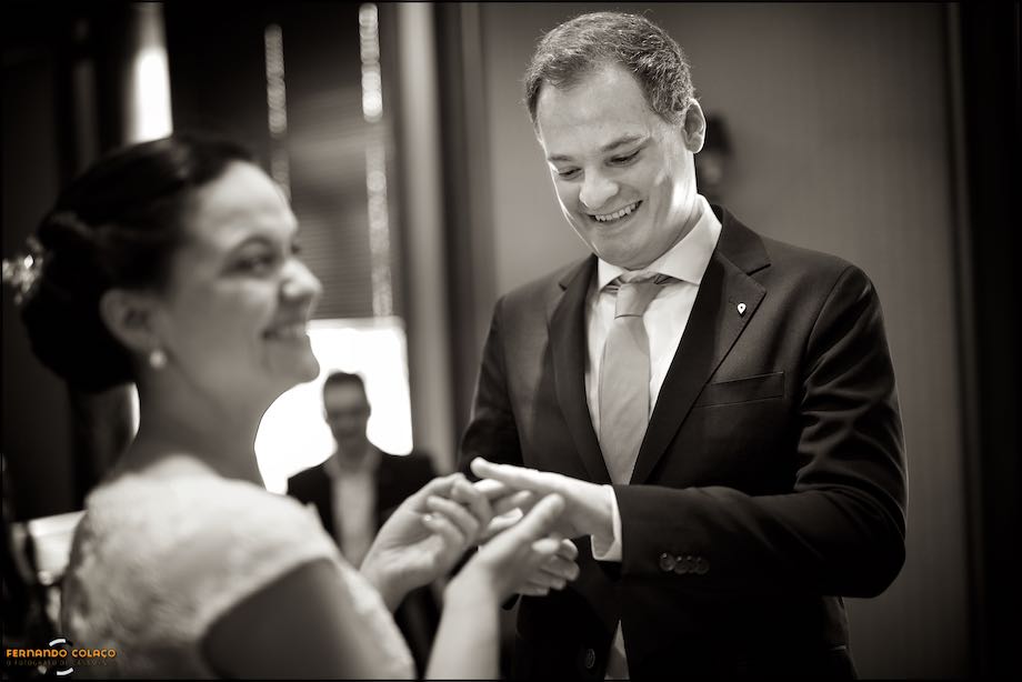 The groom, smiling, looks at his hand after receiving the ring from the bride at the wedding ceremony in Hotel Palácio Estoril.