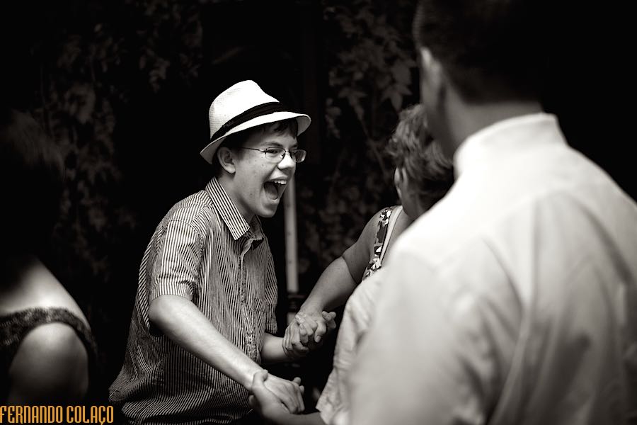 A wedding guest, wearing a hat, dances hand in hand with others, laughing a lot, in a moment captured by the wedding photographer in Lisbon.
