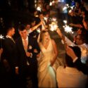 The groom and bride walk towards the wedding cake amidst golden light from glowing sticks held by guests, seen by the wedding photographer at Quinta do Castro in Cadaval.