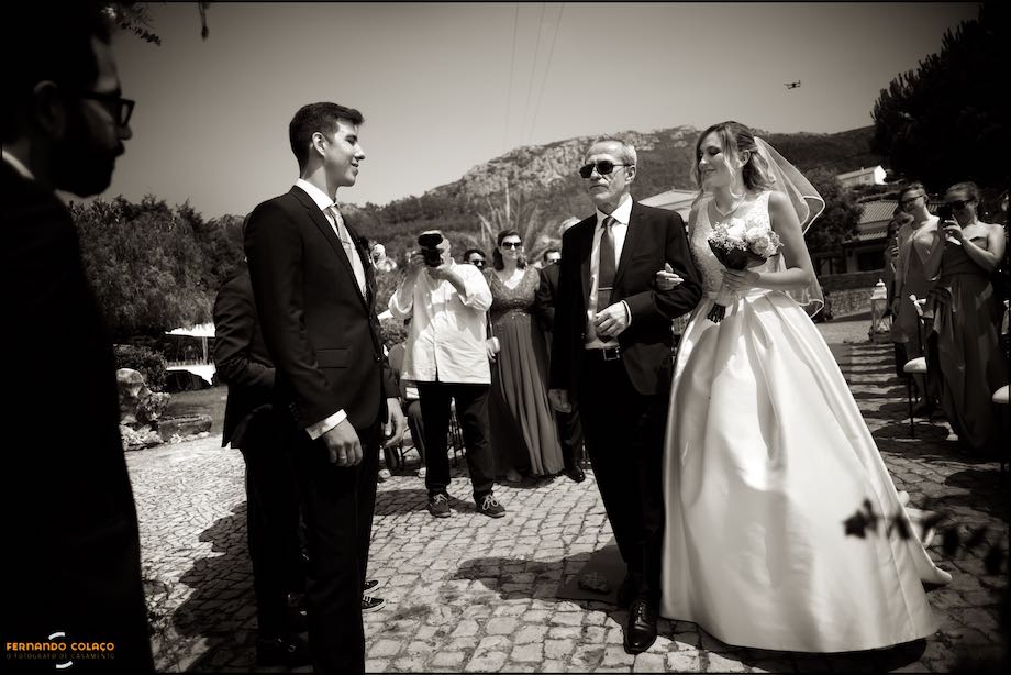 The bride is arm in arm with her father at the moment she arrives near the groom in the ceremony place in Quinta do Castro in Cadaval.