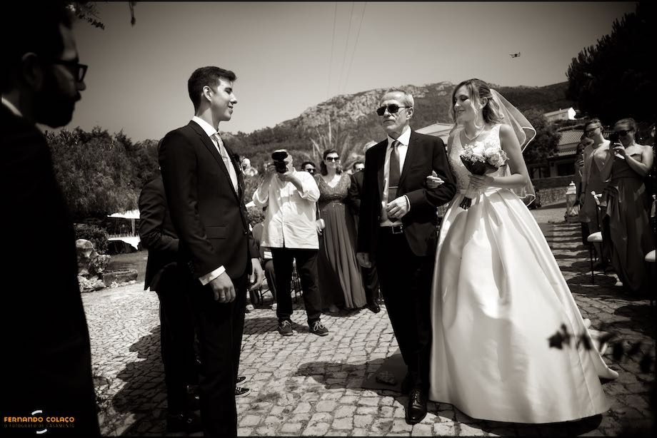 The bride is arm in arm with her father at the moment she arrives near the groom in the ceremony place in Quinta do Castro in Cadaval, seen by the Lisbon wedding photographer.