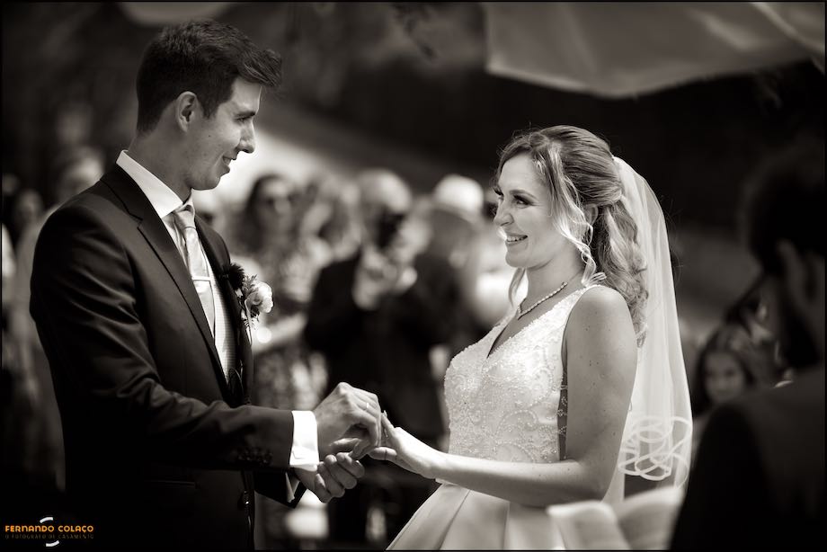 Facing and looking at each other, the groom hands the wedding ring to the bride during the wedding ceremony at Quinta do Castro in Cadaval.