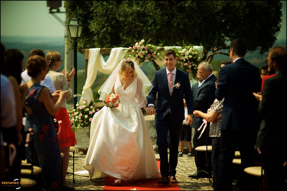 The bride and groom, holding hands, start to leave the wedding ceremony through the guests.
