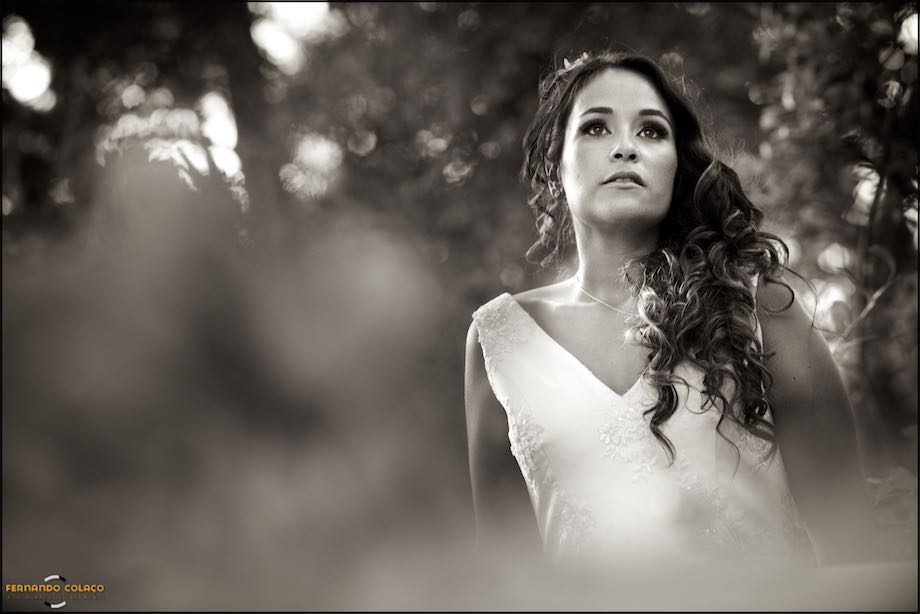 Portrait of the bride looking away among the blurry branches of the trees in the garden of Quinta da Cascata in Mafra, during the session with the wedding photographer in Lisbon.