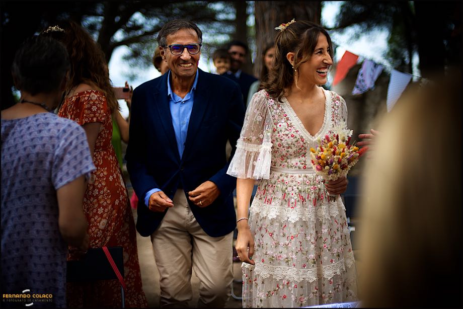 The bride and her father enter the wedding ceremony venue laughing hard amongst family members.
