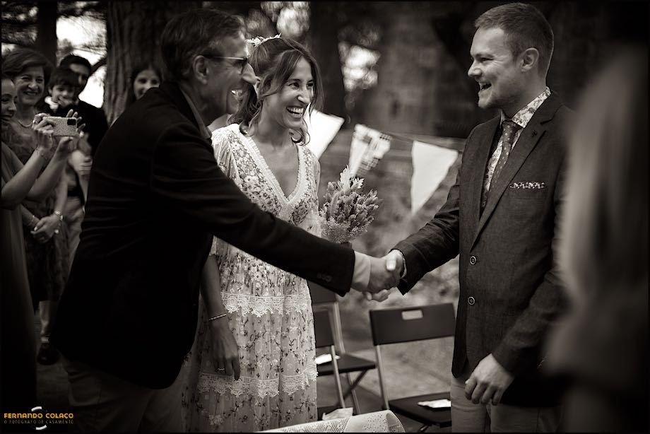 The bride's father shakes hands with the groom, with her in the center laughing with great joy, as they arrive for the ceremony, at S. Jorge Castle in Lisbon.