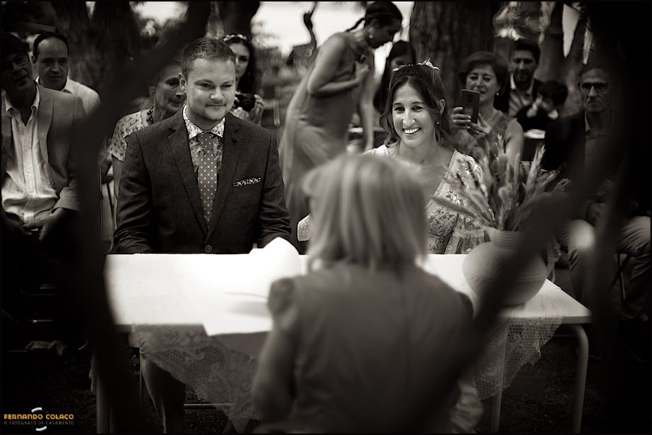 The bride and groom, next to each other, sitting at the ceremonial table with the registrar in front and family members behind.