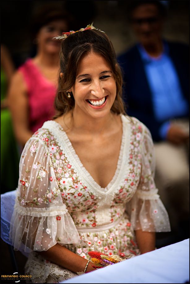 The bride, seated at the wedding ceremony table, giggles with joy at one part of the event.