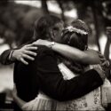 Several arms embracing the bride as they are being photographed by a guest after the wedding ceremony, seen from behind by the wedding photographer at St George's Castle in Lisbon.