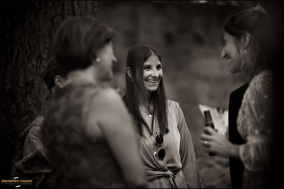 The bride's sister laughing at her who is chatting alongside her mother as they socialize following the wedding ceremony at St George's Castle in Lisbon, by the wedding photographer in Lisbon.