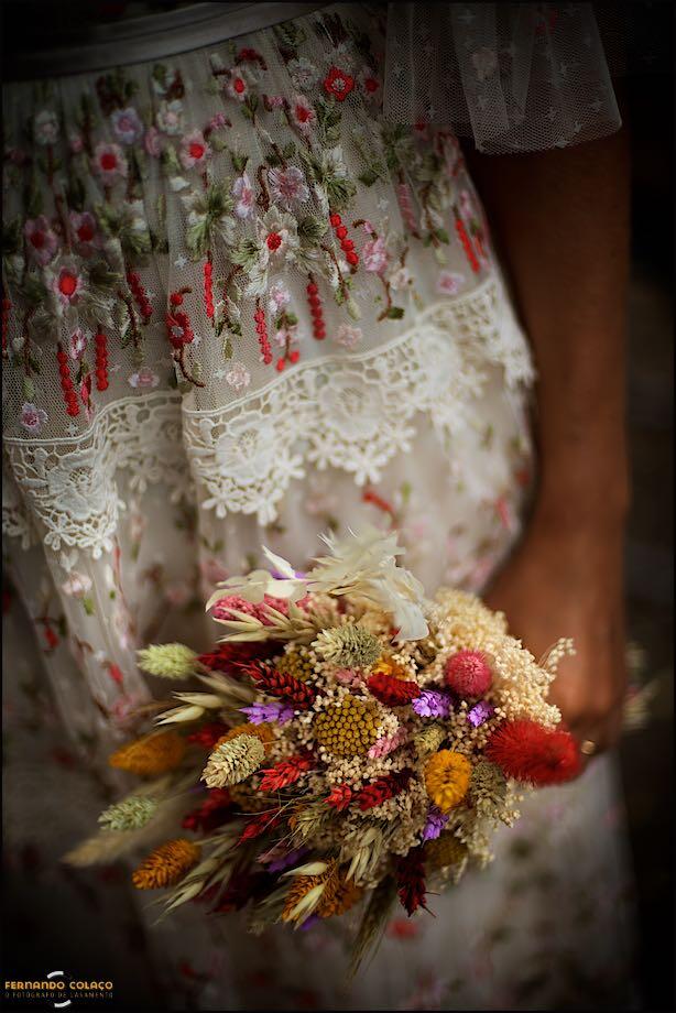 The bride's bouquet in her hand, with details of the dress, captured by the Lisbon wedding photographer.