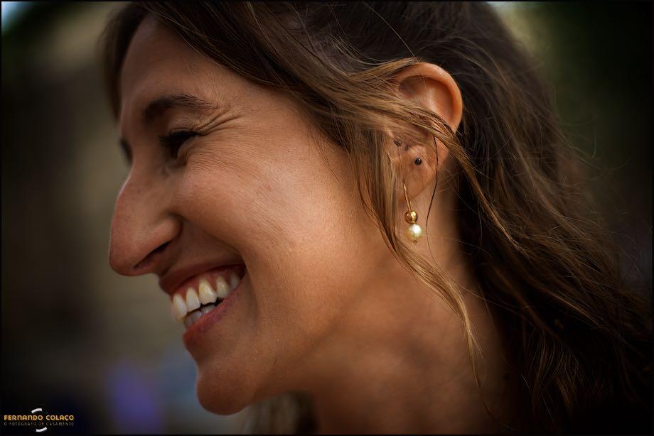 The face of the bride, seen in profile, laughing with joy at the gathering after the wedding ceremony, showing the wedding photographer in Lisbon the earring.