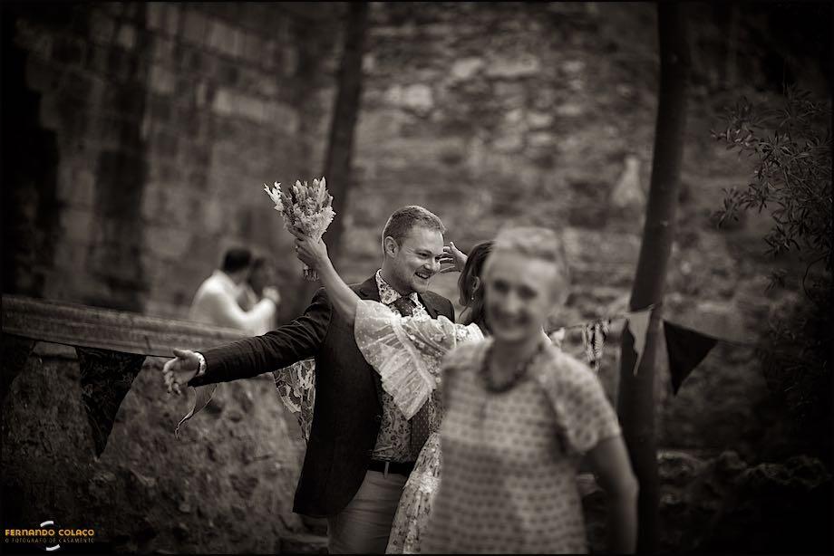 The groom opens his arms to the bride who arrives next to him, with his mother in front, blurred, in a moment captured by the wedding photographer in Lisbon.