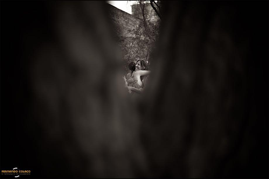 In the middle of the vertex made by the trunks of two trees, the bride hugs a friend who congratulates her on the wedding, captured by the wedding photographer in Lisbon.
