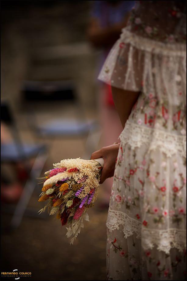 With her hands behind her back, the bride holds the bouquet that the Lisbon wedding photographer captured, along with details of the dress.