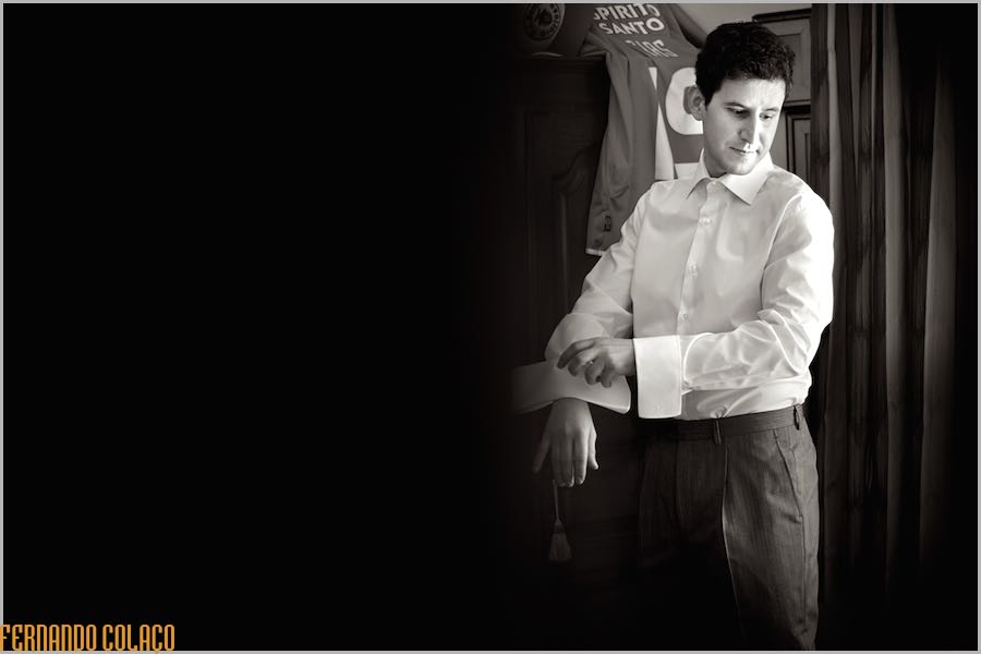 The groom, looking away as he tightens the cuff of his shirt while getting dressed for the ceremony.
