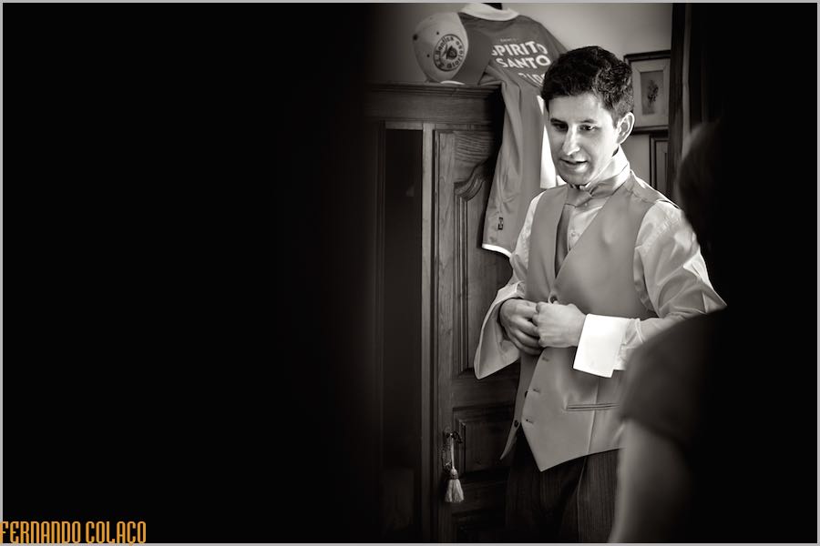 Seen from outside, the groom tightens the waistcoat of his suit, next to his mother, back and blurry, to get ready for the ceremony.