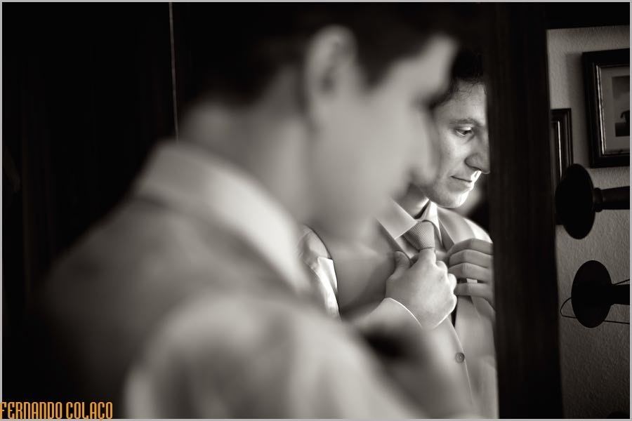 With his face in profile, his side blurred, reflected in a mirror, the groom tightens the knot of his tie, in preparation for the ceremony.