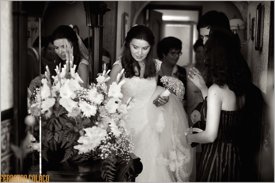 The bride with family members just gets ready to leave the house to go to the ceremony, next to a mirror that reflects her.