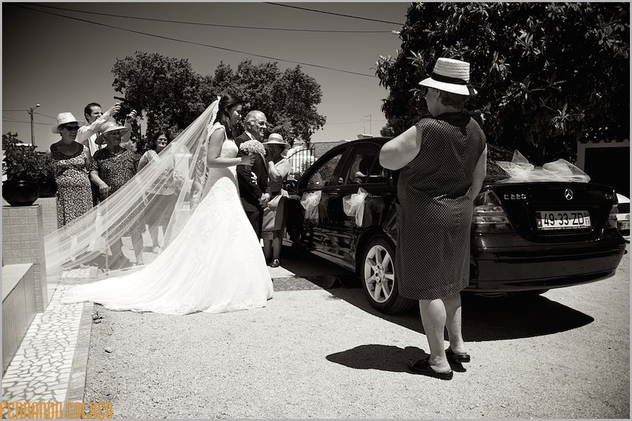 In the street, the bride gets ready to get in the car with the help of her father, seen by neighbors wishing her well.