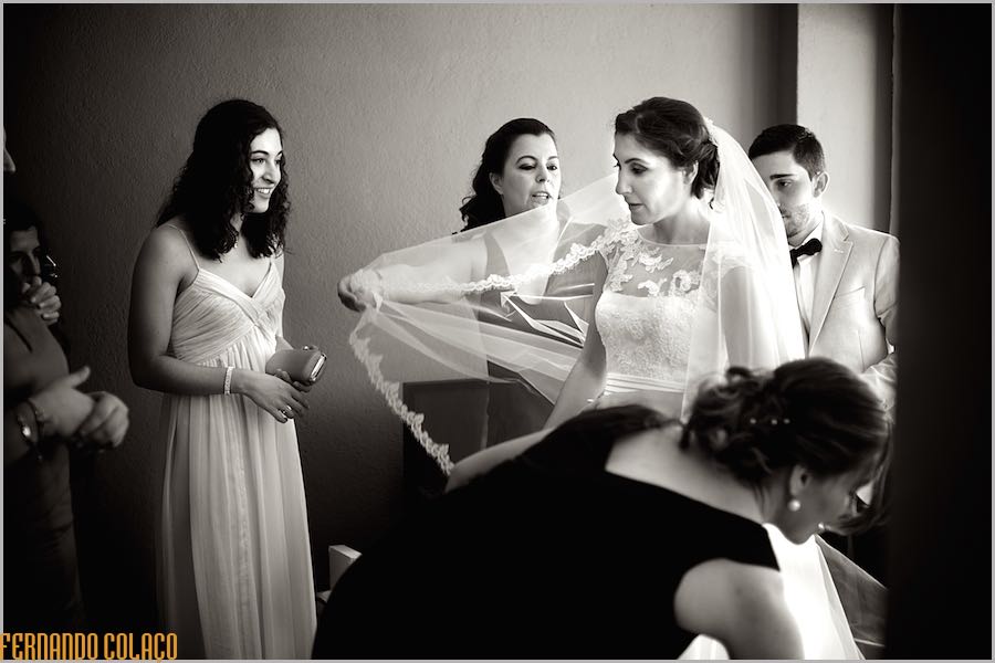 The bride amongst friends and family helping her with her dress, in a composition by the wedding photographer in Lisbon.