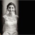 Ready to leave for the ceremony, the bride smiles in a portrait within a crack of light that the wedding photographer took advantage of.