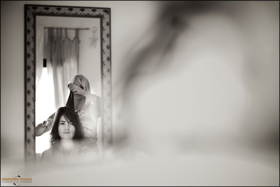 In a mirror with a large decorated frame, the bride being styled by her hairdresser as she prepared for her wedding day, spotted by the wedding photographer in Sintra.