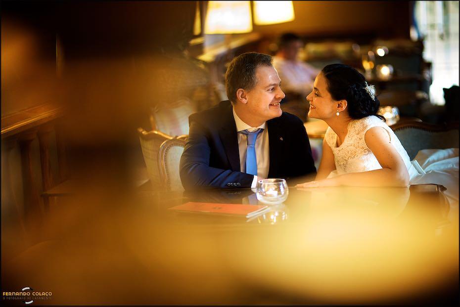 Sitting in the bar of the Palácio Estoril Hotel, the bride and groom smile at each other during their photo session with the wedding photographer in Cascais.