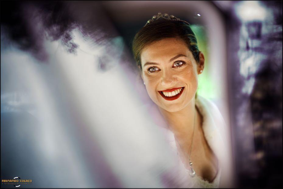 A noiva sorri de dentro do automóvel, por entre reflexos desfocados nos vidros da janela, em composição do fotógrafo de casamento em Lisboa.