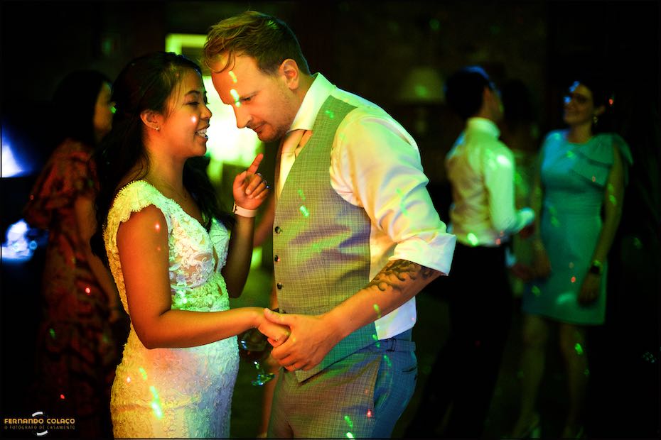 The groom and the bride, under the yellow and green light of the Agostos dance floor, open the dance floor at the party, as seen by the Algarve wedding photographer.