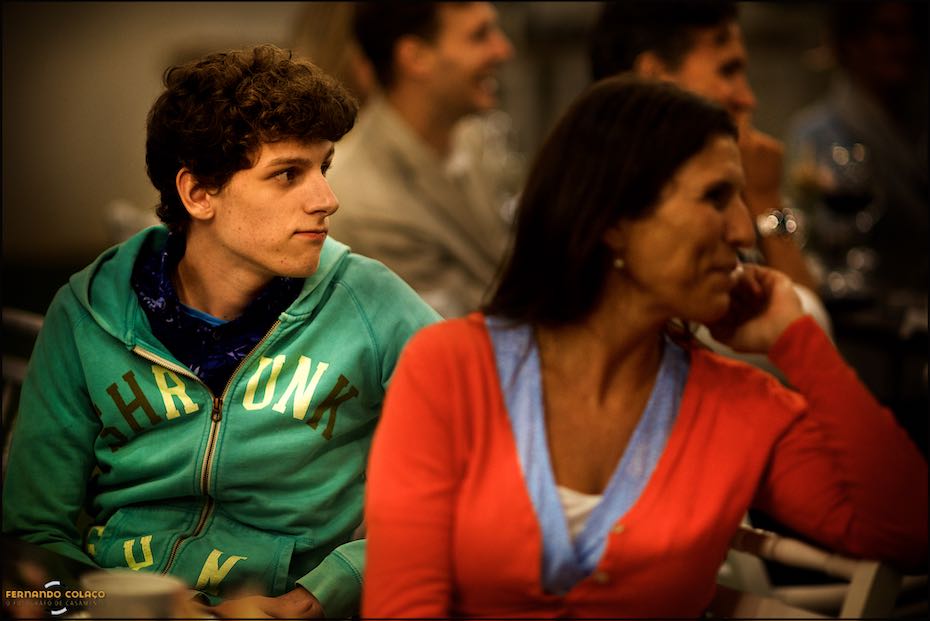 A boy, sitting next to his mother, looks away to listen carefully to a speech at a wedding in Agostos, captured by a wedding photographer in the Algarve.
