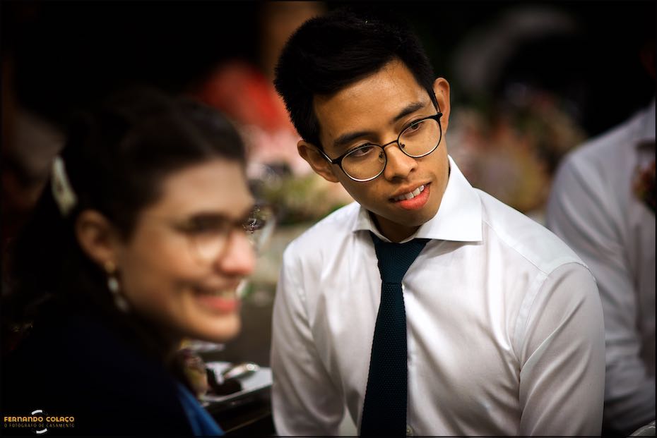 A wedding guest, next to his girl friend, out of focus, listens attentively to a speech at the wedding dinner in Agostos, Algarve.