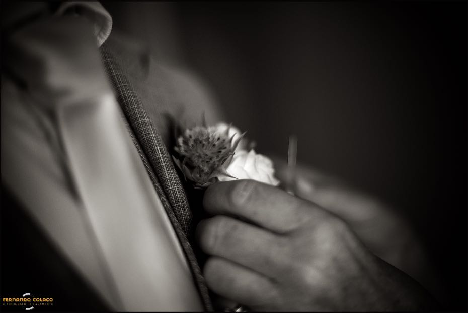 Detalhe com as mãos da mãe do noivo a pôr a flor na lapela do casaco do filho, numa composição pelo fotógrafo de casamento no Algarve.