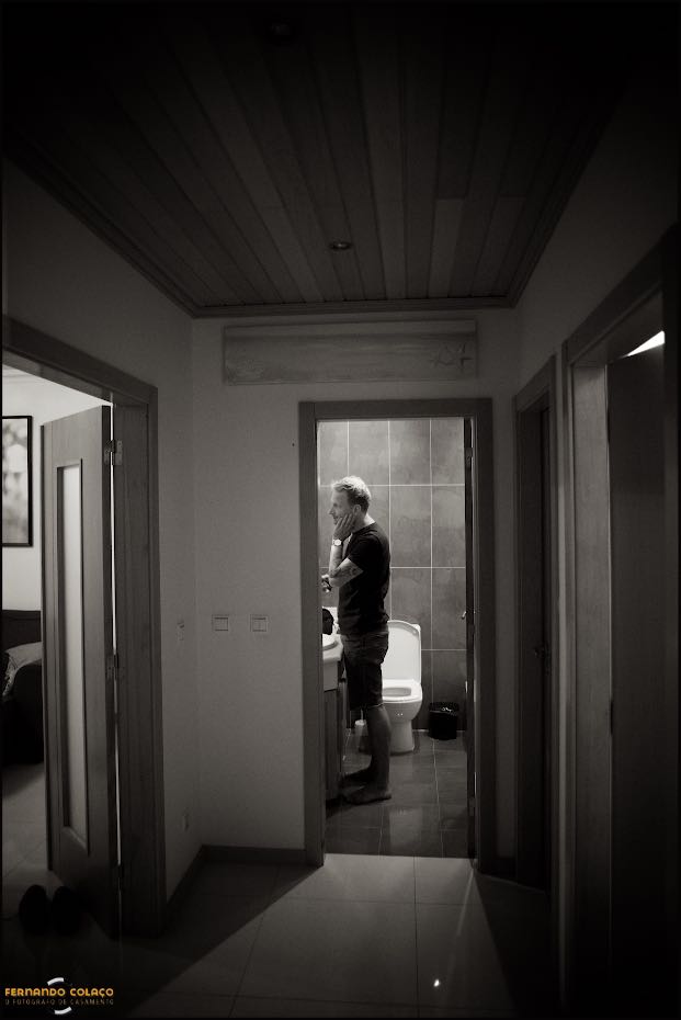 Ao fundo do corredor, o noivo barbei-se ao espelho.