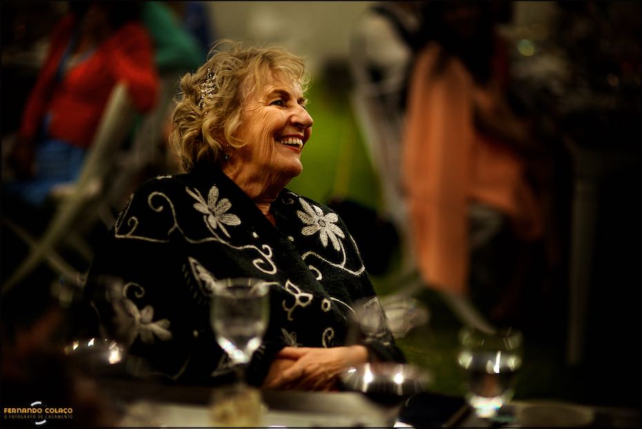 A mãe do noivo ri com satisfação ao ouvir um discurso na festa do casamento nos Agostos, capturada pelo fotógrafo de casamento no Algarve.