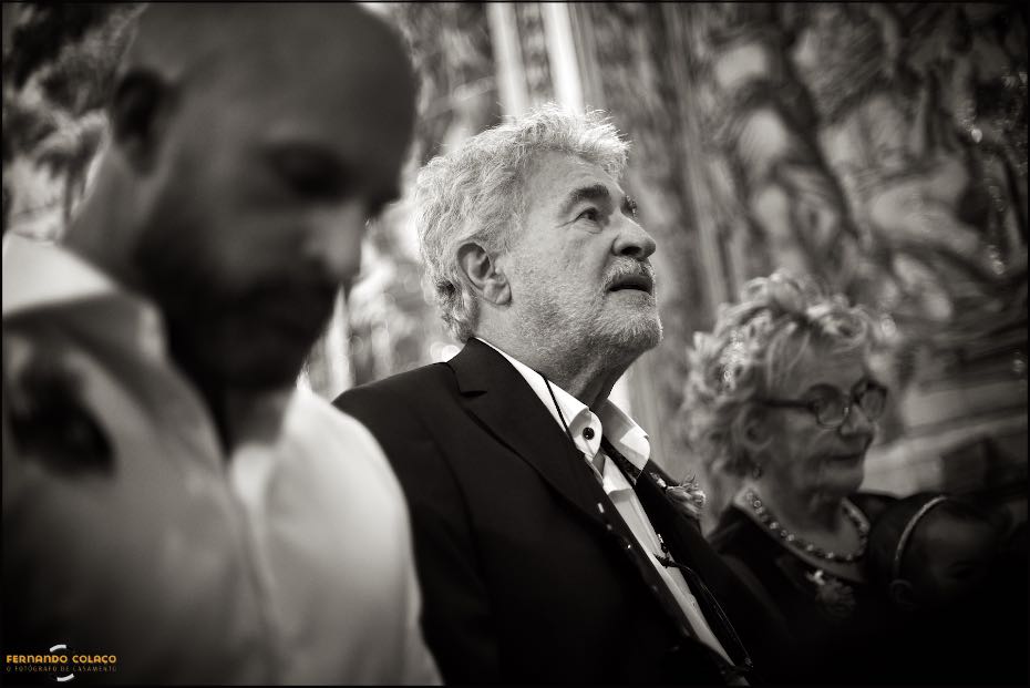 O pai do noivo, entre o irmão e a mãe, desfocados, quando assiste ao desenrolar da cerimónia do casamento na Igreja de S. Lourenço em Almancil.