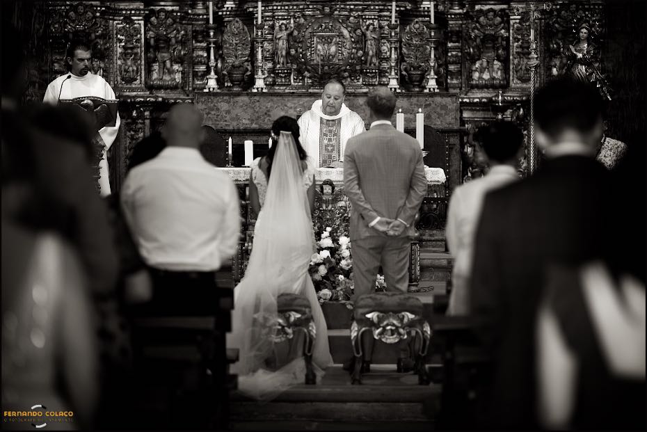Vistos por detrás, com o padre e o sacristão no altar da Igreja de S. Lourenço em Almancil, os noivos numa das partes da cerimónia do casamento.