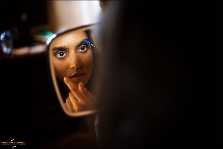 Num pequeno espelho, o fotógrafo de casamento em Évora capta o rosto da noiva acertando as sobrancelhas, quando se prepara para o casamento no Convento do Espinheiro em Évora.