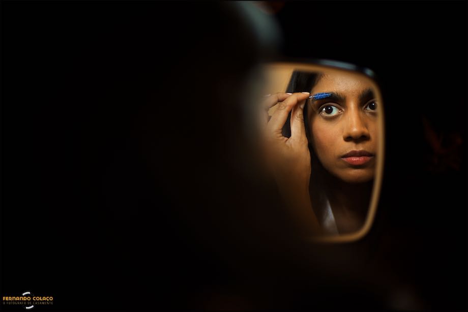 Detalhe do rosto da noiva num espelho, quando ela acerta as sobrancelhas ao preparar-se para a cerimónia no Convento do Espinheiro em Évora, vista pelo fotógrafo de casamento.