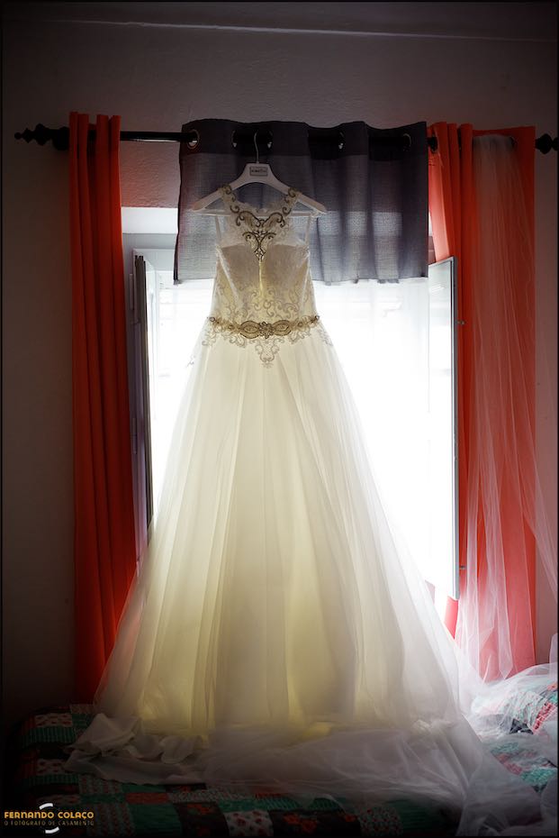 O vestido da noiva pendurado numa janela mostrando a luz que o atravessa, numa composição do fotógrafo de casamento em Évora.