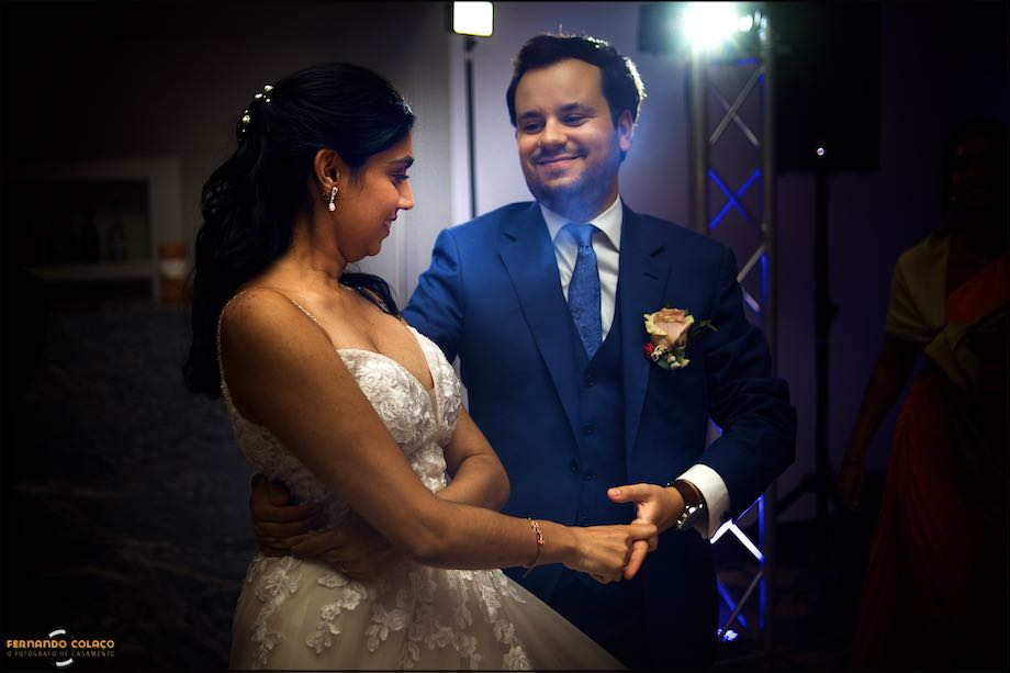 Os noivos, de frente e olhando um para o outro, sorriem enquanto dançam na abertura da pista da festa do casamento.