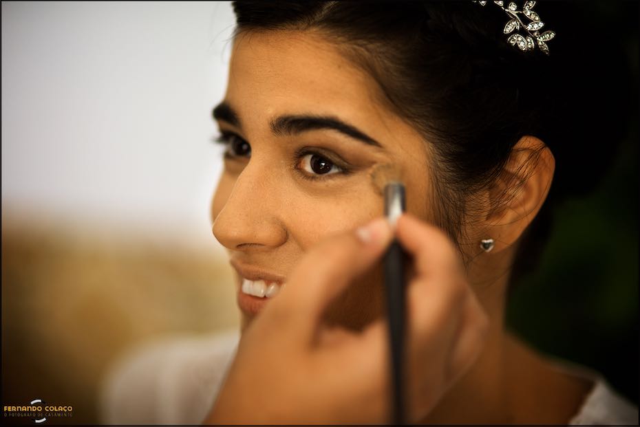Mão com pincel espalha o pó na face da noiva, quando esta se prepara para o seu casamento na Igreja Matriz de Reguengos de Monsaraz, num retrato pelo fotógrafo de casamento no Alentejo.