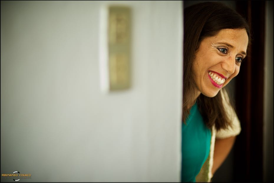 Uma amiga da noiva espreita à porta da sala onde a noiva está a ser penteada, quando se apronta para o dia do casamento