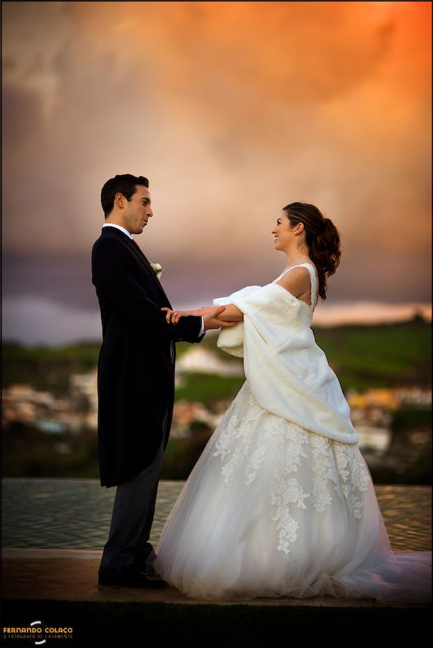 Junto da água da piscina da Casa de Reguengos, os noivos, de frente um para o outro e de mãos dadas, olham encantados um para o outro, na linda luz quente do entardecer.