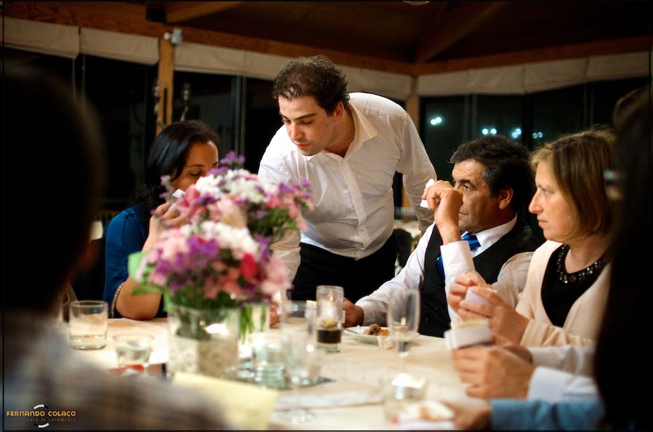 O noivo, durante o jantar da festa do casamento, mostra algo aos seus convidados sentados à mesa do jantar, na Quinta de Nossa Senhora da Serra em Sintra.